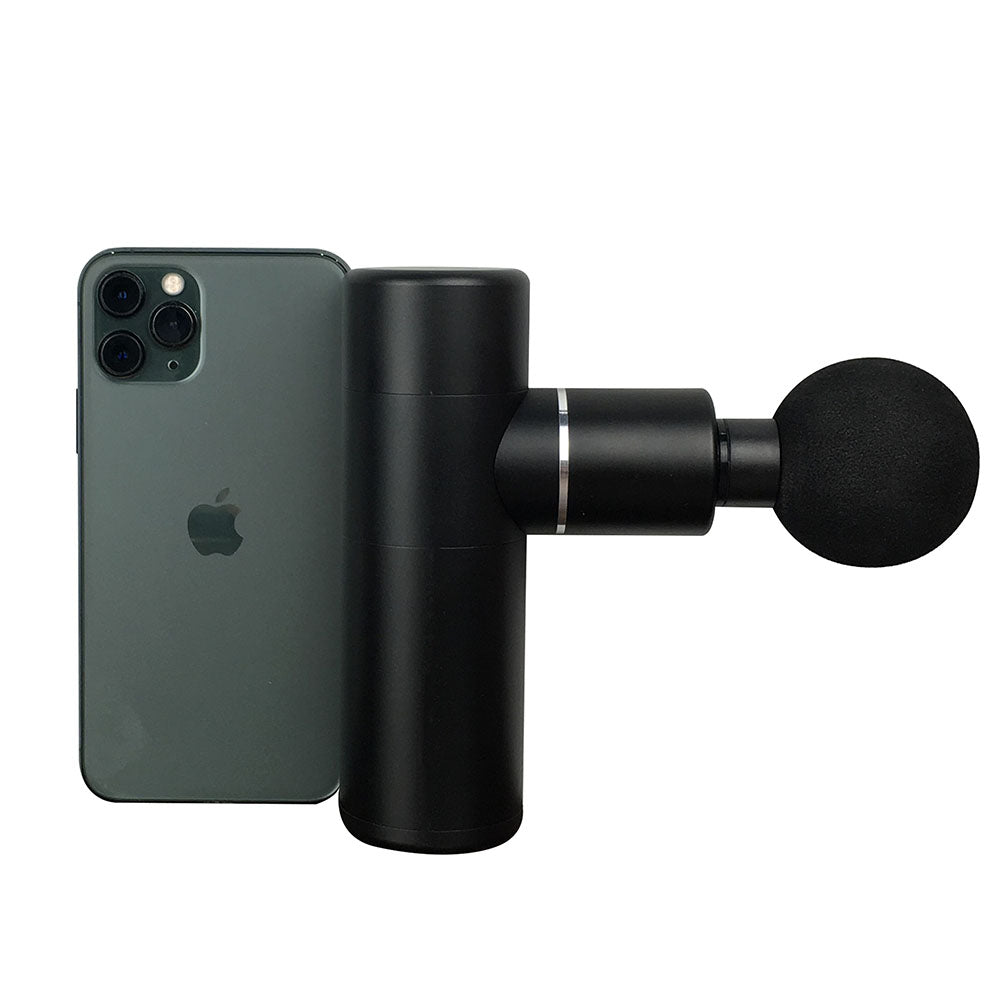 A compact and portable black massage device next to a smartphone, indicating its size and scale.